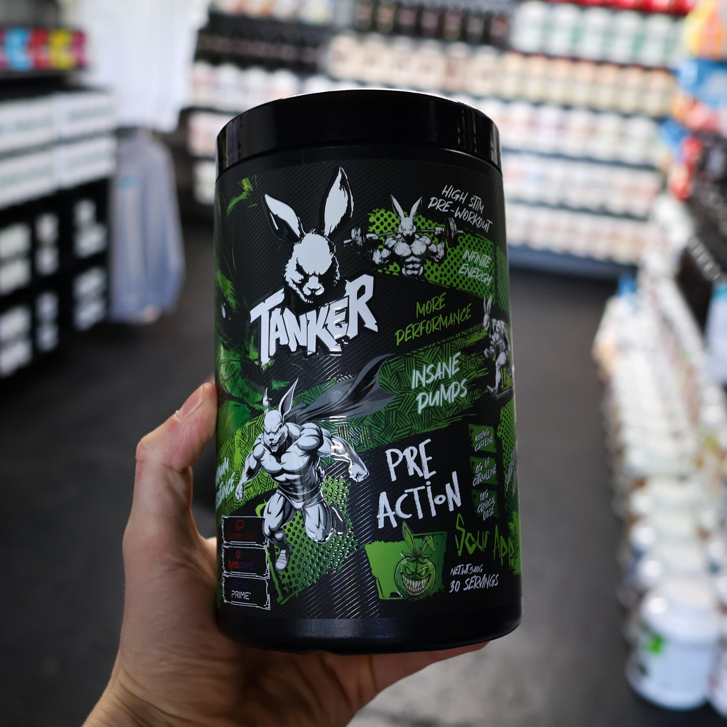 Hand holding a 'Tanker' pre-action pre workout supplement container in a store setting