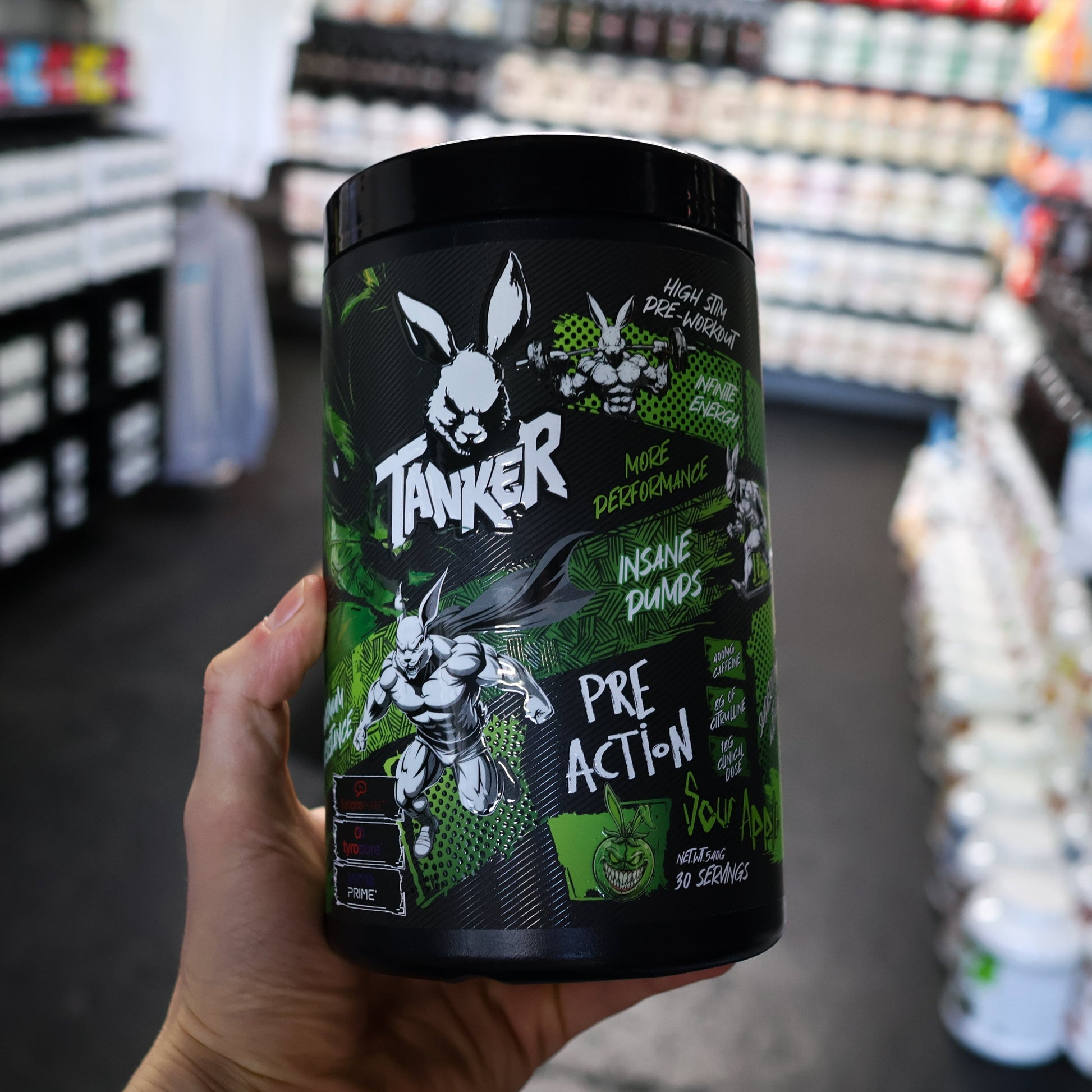 Hand holding a 'Tanker' pre-action pre workout supplement container in a store setting